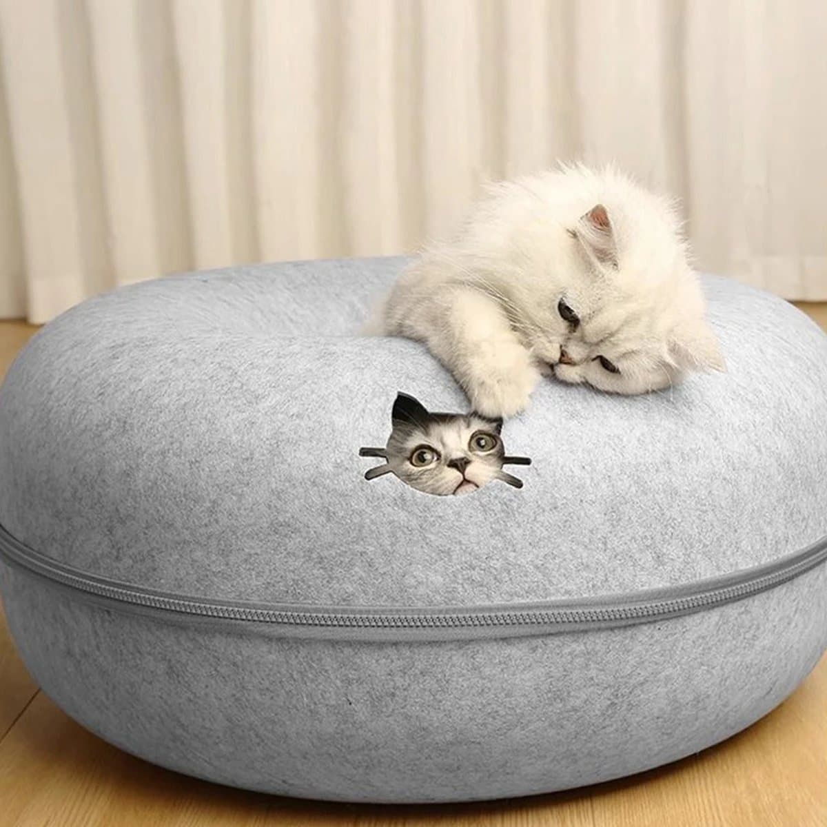 Gato blanco descansando sobre la cama cueva de fieltro gris
